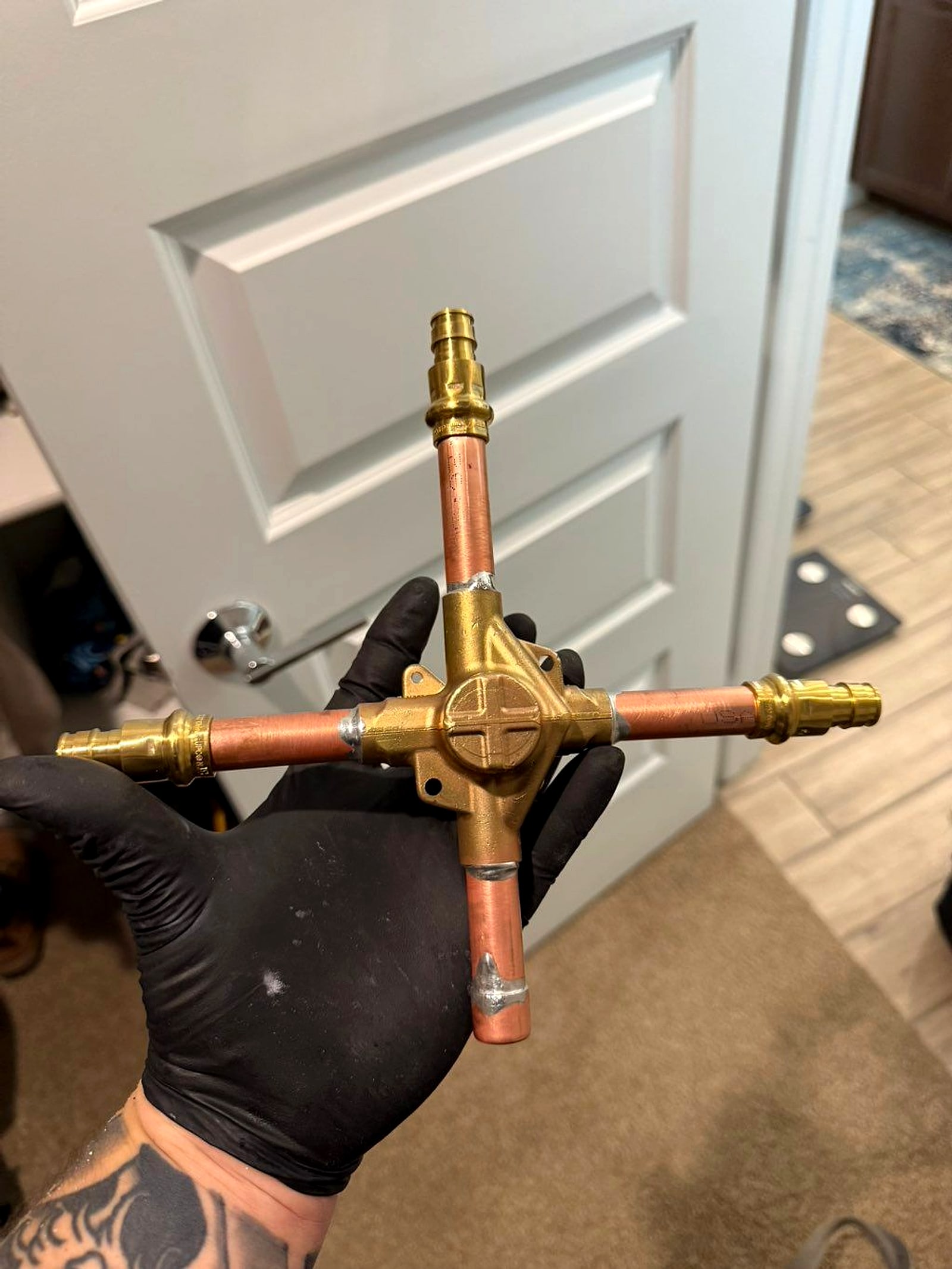 Joseph's gloved hand holding a copper valve assembly he built for a job
